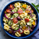 tortellini pasta salad with tomatoes, cucumbers, olives, and feta in a blue bowl