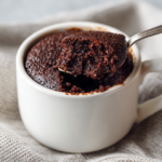 Rich chocolate mug cake in white ceramic cup with spoonful lifted