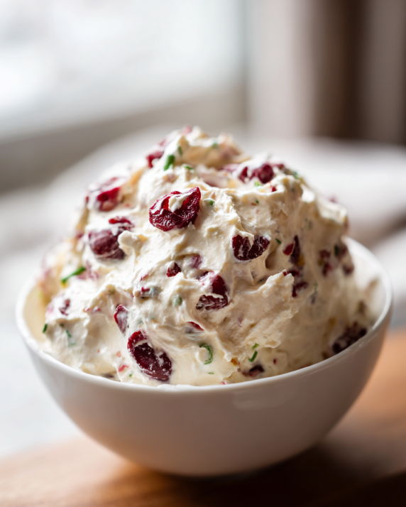 Cranberry jalapeño cream cheese dip in a white bowl with colorful cranberries and herbs